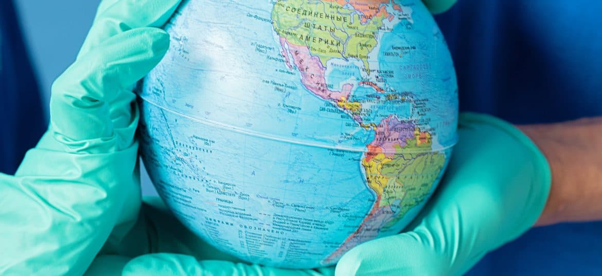 Gloved hands holding a globe to represent global health access.